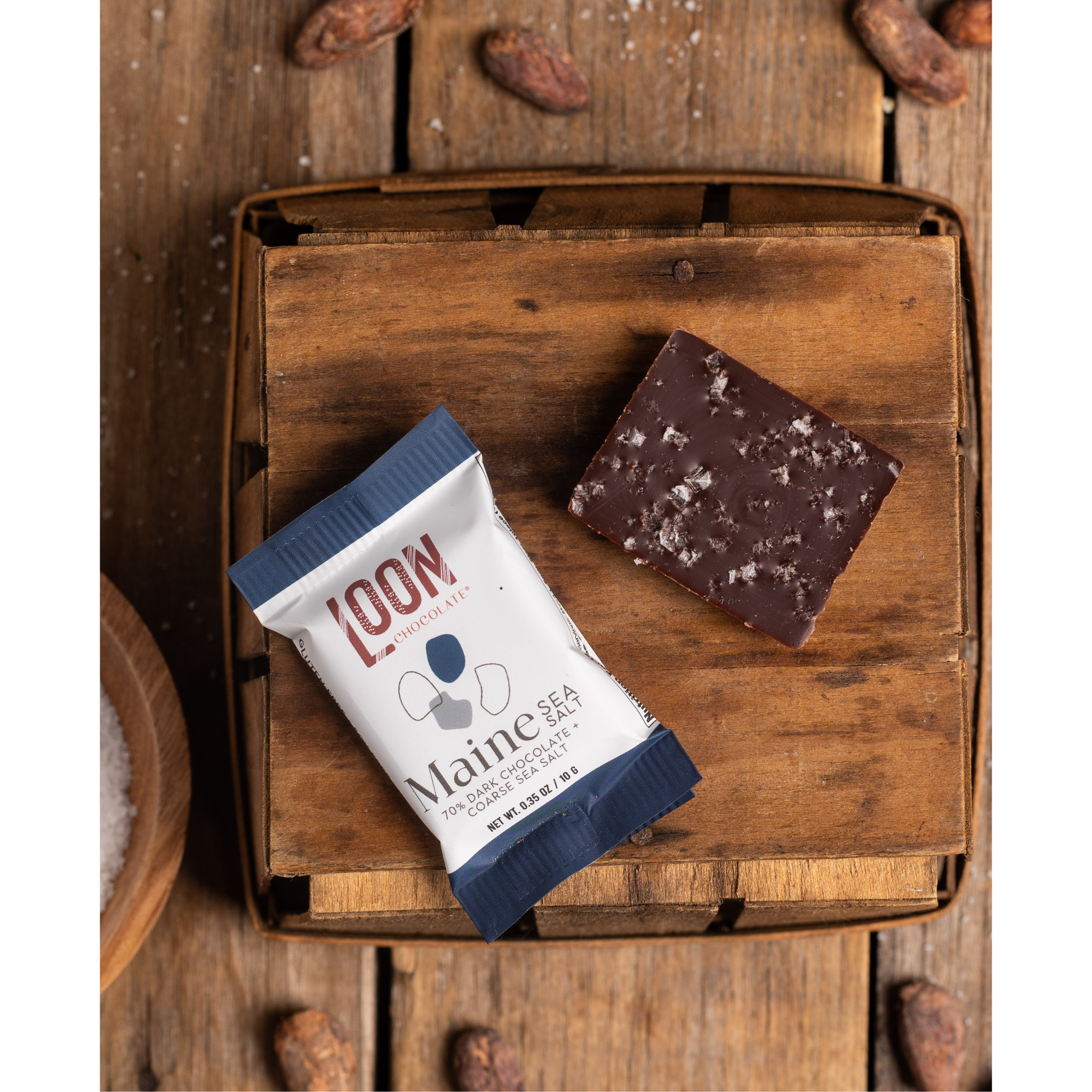 Maine Sea Salt Dark Chocolate Mini Bar by Loon Chocolate on wooden surface with cacao beans