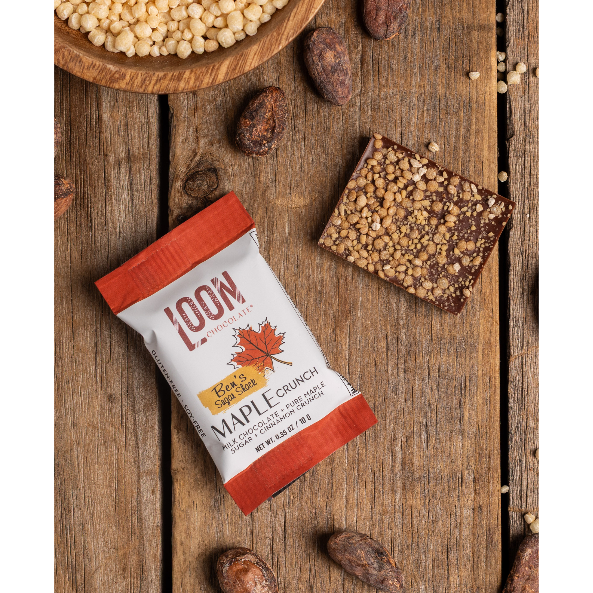 Maple Crunch Milk Chocolate Mini Bar by Loon Chocolate on wooden surface with cacao beans