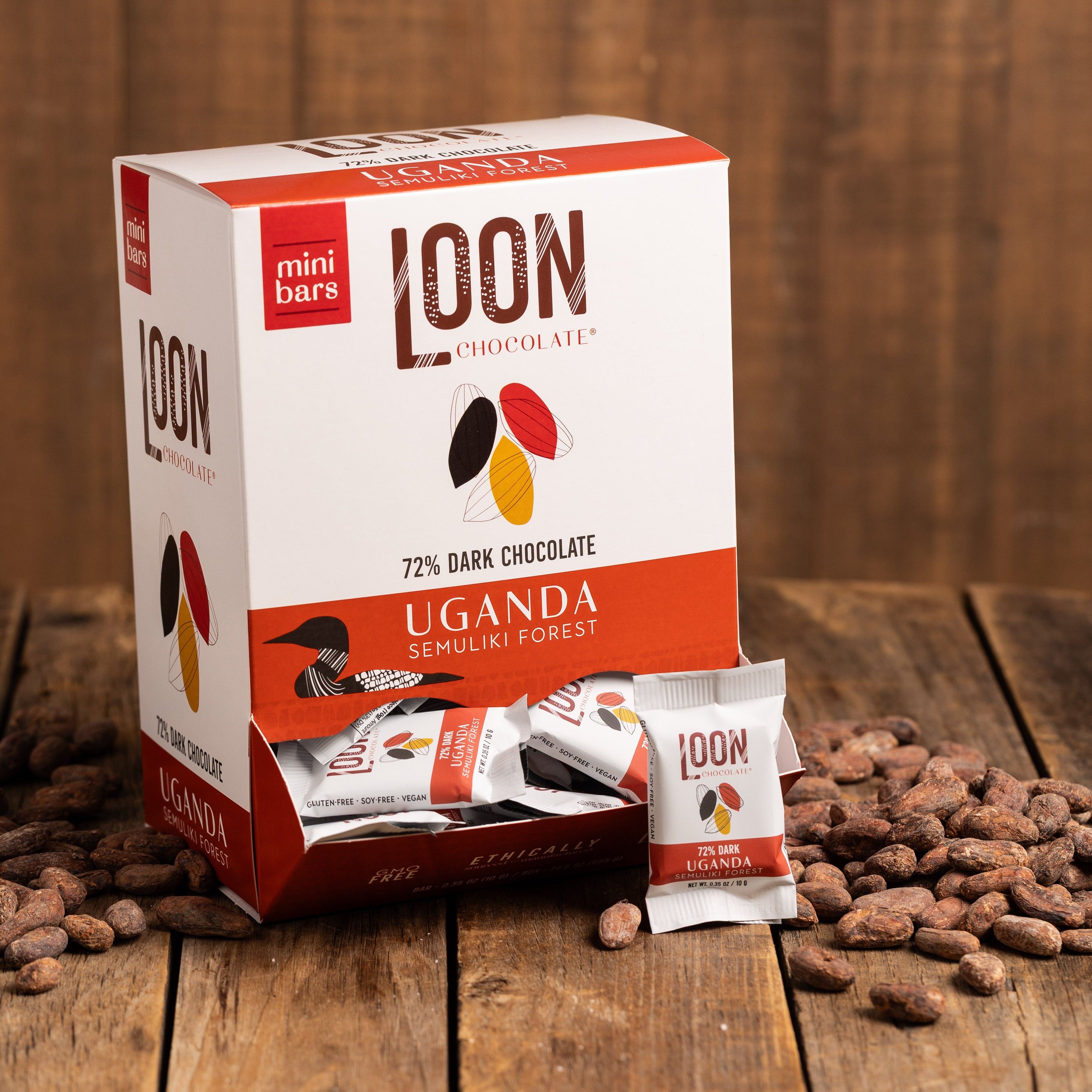 Box of 72% Uganda Dark Chocolate mini bars by Loon Chocolate on wooden surface with cacao beans
