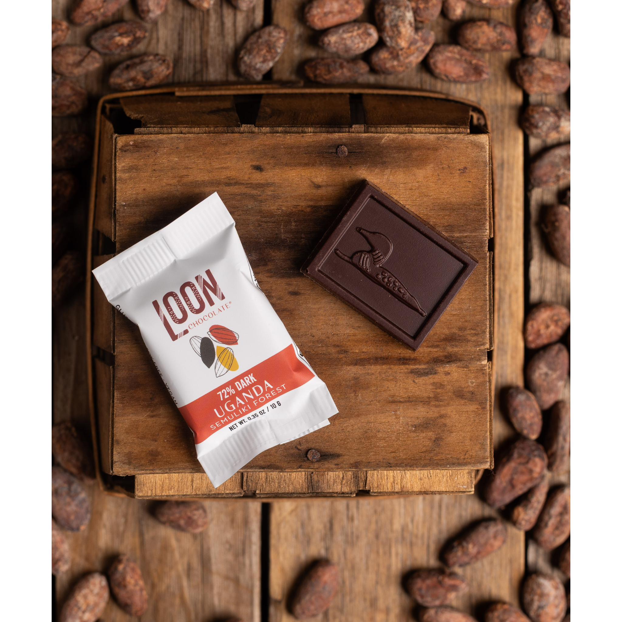72% Uganda Dark Chocolate Mini Bar by Loon Chocolate on wooden surface with cacao beans